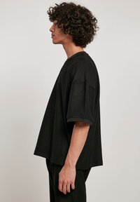 Tricou oversized negru cu mâneci scurte și decolteu la baza gâtului, având un croi lejer și un material texturat.