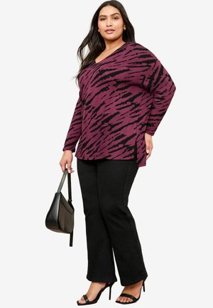 Long-sleeve top in deep plum with black tiger stripe pattern, paired with black flared jeans and black heels, holding a black handbag.