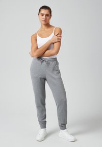 Graue Jogginghosen mit elastischen Bündchen und Kordelzugbund, kombiniert mit einem taillierten weißen Tanktop und weißen Sneakers, vor einem schlichten Hintergrund.