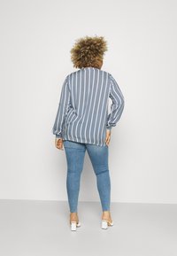 Striped blue long-sleeve blouse with a relaxed fit, paired with light blue skinny jeans and white block-heeled sandals.