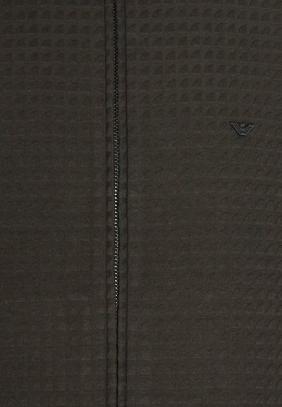 Giacca nera con zip, realizzata in tessuto testurizzato, caratterizzata da un motivo sottile, con chiusura frontale a zip e un piccolo logo vicino al colletto.