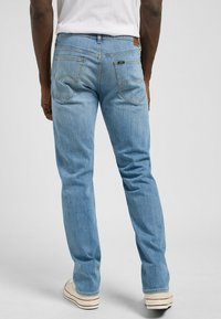 Jeans de mezclilla azul claro con un corte recto. Las características incluyen dos bolsillos traseros, un sutil diseño de marca y costuras en contraste.
