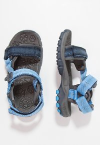 Modré a šedé dětské sandály s textilními pásky a gumovou podrážkou. Na stélce je vzor v podobě otisků tlapek a podrážka má texturovaný povrch.
