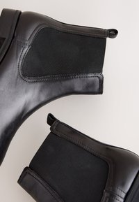 Zwarte leren enkellaarsjes met elastische zijpanelen, een ronde neus en een getextureerde afwerking, voorzien van een lusje voor gemakkelijk aantrekken.