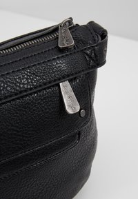 Borsa a mano in pelle nera con finitura texturizzata, chiusura superiormente con zip e accessori in metallo con incisioni. Forma compatta e arrotondata.