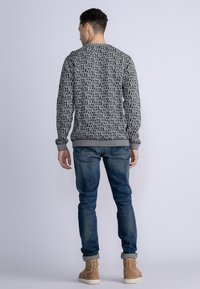 Hanorac cu un model alb-negru, guler rotund, manșete și talie ribbate, purtat cu blugi blue și cizme până la gleznă bej.