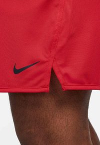 Czerwone spodenki sportowe z teksturowanej tkaniny, z czarnym logo Nike na końcu i bocznym rozcięciem dla większej swobody ruchu.