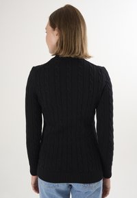 Pull en maille noire avec un motif texturé, doté de poignets et d'un ourlet côtelés, et d'une coupe ajustée. La vue arrière montre un col montant.