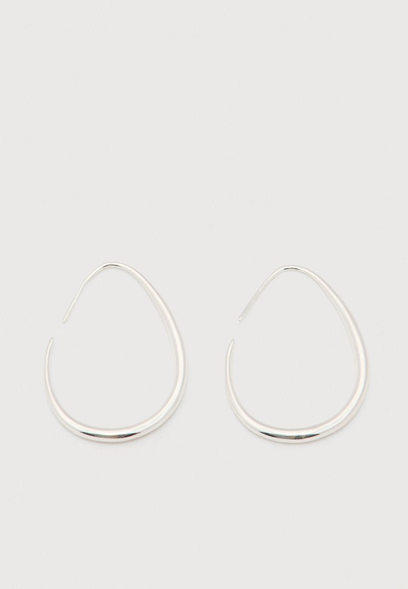 Para gładkich, srebrnych kolczyków w kształcie otwartych kropli łzy z cienkimi zapięciami na druciku na jednolitym białym tle.