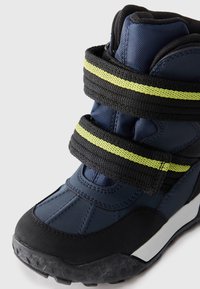 Marine wandelschoen met een zwarte rubberen zool, gestructureerd synthetisch bovenwerk, gele gestreepte klittenbandriemen en gevoerde enkelsupport.