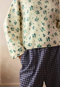 Kootud kampsun heleda kollase värviga, sinise ja rohelise lillemustriga, kombineeritud lõdva sinise ruudulise pükstega. Tekstuuriga kangas, ribaga äär.