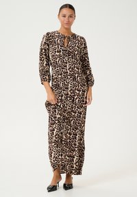 Robe maxi en imprimé léopard, manches longues, détail au niveau de l'encolure en forme de clé, tissu léger, poches latérales, assortie à des chaussures à talons noires.