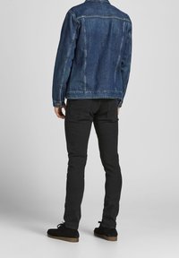 Chaqueta vaquera azul medio, diseño ajustado con mangas largas y bolsillos en el pecho, combinada con pantalones negros ajustados y zapatos de ante negros.