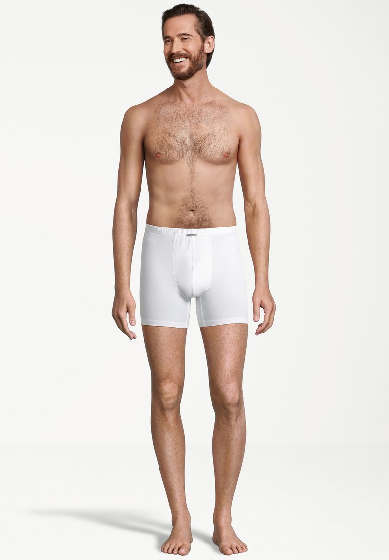 Boxers en coton blancs avec une taille mi-haute et une ouverture à l'avant, portés par un mannequin masculin avec un torse nu et des cheveux courts.