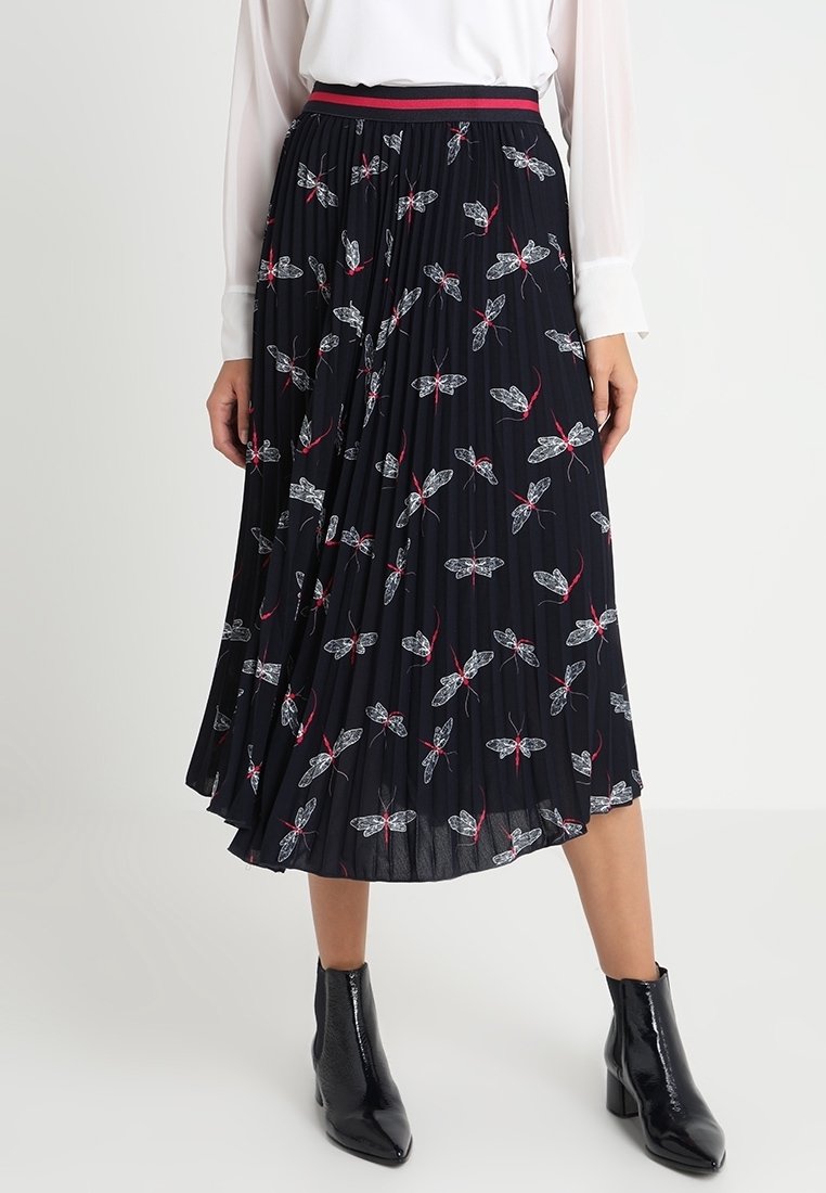 Zwarte geplisseerde rok met een wit en rood bloemmotief, voorzien van een rood en zwarte tailleband, gestyled met zwarte enkellaarsjes.