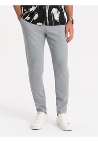 Šedé joggingové kalhoty s texturovaným povrchem, navržené v slim fit střihu. V kombinaci s bílými teniskami na neutrálním pozadí.
