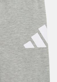 Pantalones deportivos grises con una textura suave, que presentan un diseño de logo de tres rayas blancas en la parte inferior de la pierna izquierda.