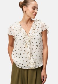 White floral blouse with ruffled neckline and short sleeves; features small brown and green flower patterns; lightweight, flowy fabric.