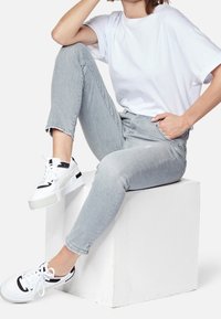 Jeans de color gris claro con un ligero estiramiento, una camiseta blanca de manga corta y zapatillas de plataforma en blanco y negro sobre un pedestal blanco.