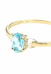 Anillo de oro con una gema azul ovalada, engastada en cuatro garras, con una banda lisa y grabado "9ct" en el interior.