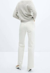 Jean droit blanc en denim, avec deux poches arrière, couture visible et un pull gris texturé, porté à la taille.