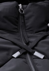 Svart vadderad jacka med hög krage, utrustad med en metalldragkedja och texturerade svarta snoddar. Slät tyg med minimala detaljer.