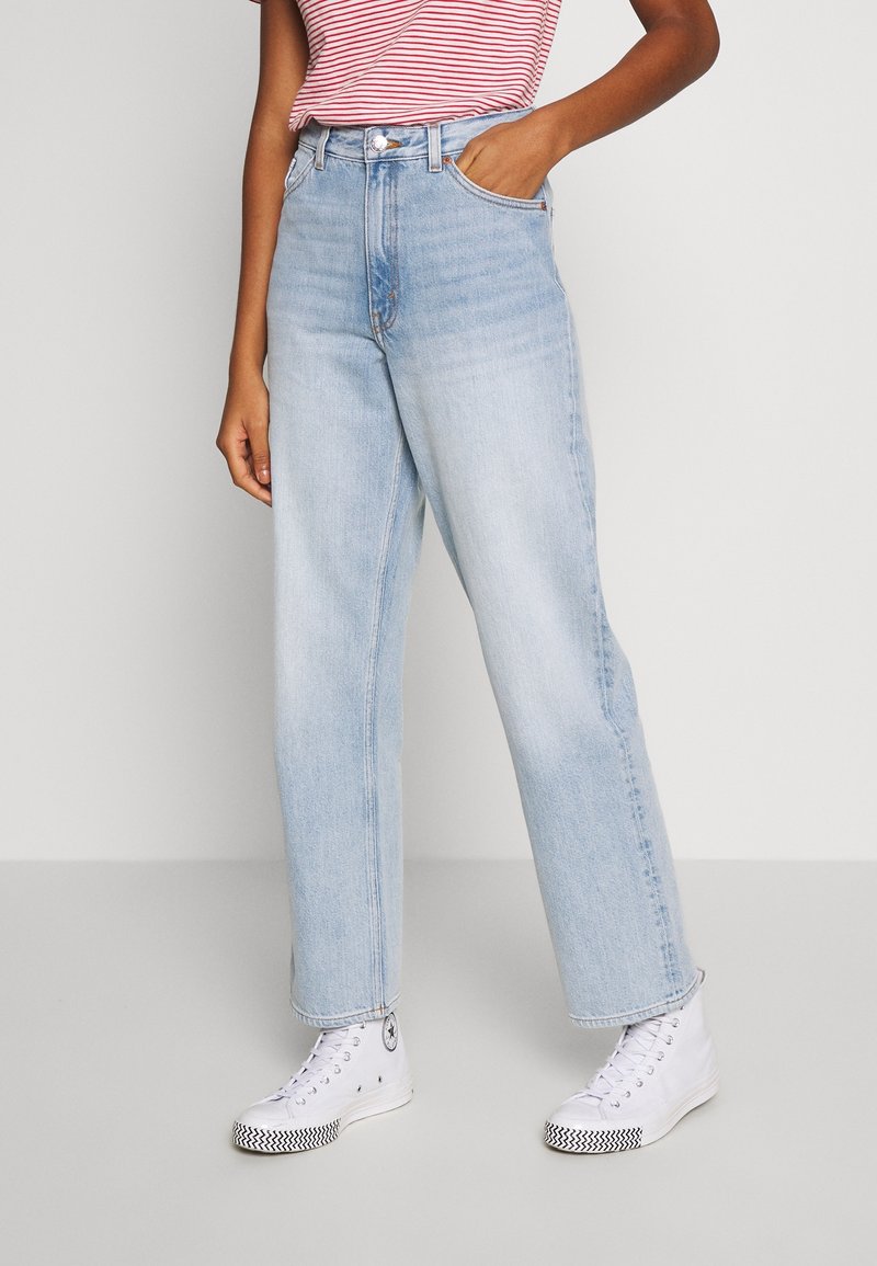 Jeans taille haute bleu clair avec une coupe droite, dotés de cinq poches et d'un léger effet délavé, associés à des baskets blanches.