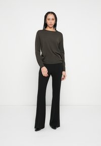 Top de manga larga de color verde oscuro combinado con pantalones acampanados negros. El conjunto está confeccionado con tela suave, presenta un ajuste relajado y un diseño minimalista.
