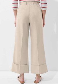 Beige weite Hosen mit hoher Taille, glatter Textur und umgeschlagenen Säumen. Zwei hintere Taschen sind sichtbar.