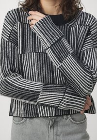 Maglione a maglia a strisce bianche e nere con un motivo testurizzato, dotato di scollatura a girocollo e polsini a coste, abbinato a jeans denim grigio chiaro.