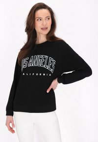 Sudadera negra de manga larga, con "LOS ÁNGELES" y "CALIFORNIA" impresos en blanco. Corte casual, cuello redondo, textura suave.