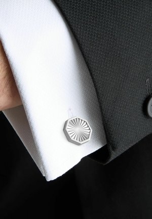 Close-up of a white dress shirt cuff with a silver octagonal cufflink and a black suit sleeve.