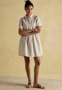 Lühikeste varrukatega puuvillane kleit roosa ja rohelise lillemustriga, kraega disain ja laienev seelik. Kanda beežide sandaalidega.