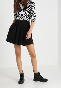 Zwarte corduroy rok met plooien en een elastische tailleband, gecombineerd met een zwart-wit gestreept sweater met zebra-print en zwarte veterschoenen tot de enkel.