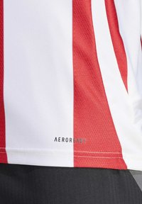 Rood-witte gestreepte sporttrui. Gemaakt van ademend materiaal met een gladde textuur. "AEROREADY" logo gedrukt aan de onderkant.