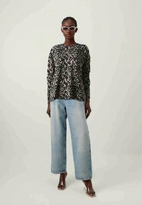 Løs passform genser med et mørkt mønster og lyse detaljer, sammen med lyseblå vide jeans og gjennomsiktige hælsandaler. Hvit solbriller.