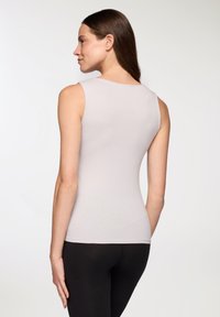 Top senza maniche di colore grigio chiaro realizzato in tessuto elasticizzato, con scollatura tonda e silhouette aderente, abbinato a leggings neri.