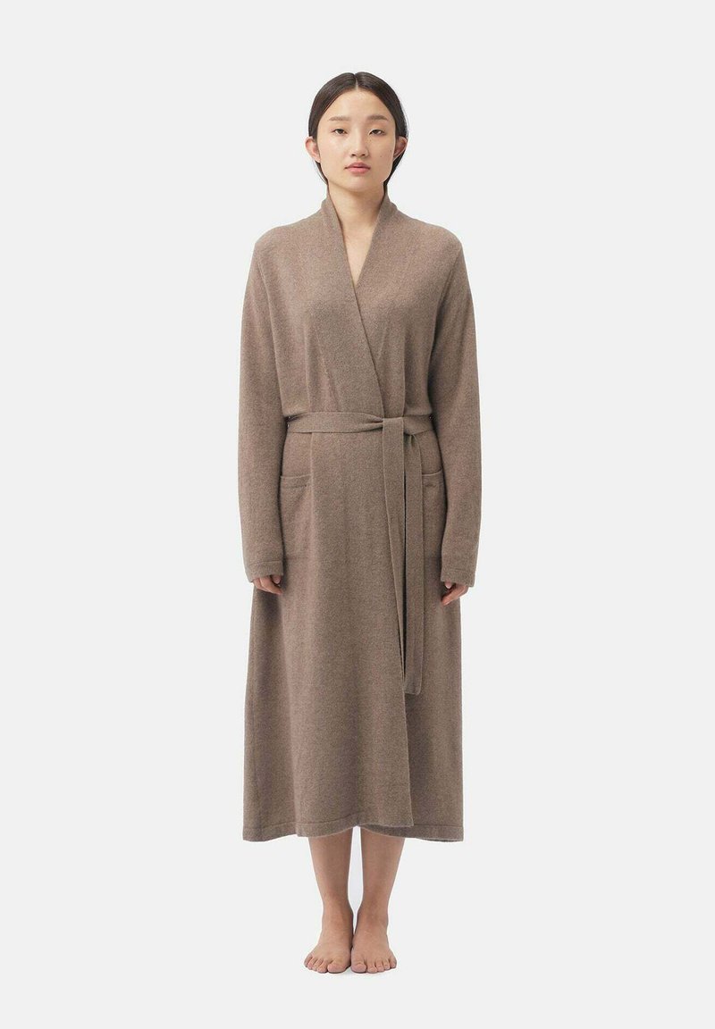 Robe marron à manches longues de style enveloppant, fabriquée dans un matériau doux, dotée d'une ceinture à la taille et de deux poches latérales. Texture lisse.