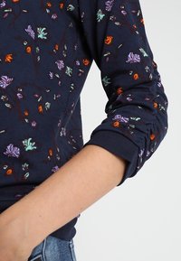 Maglione navy con motivi floreali in viola, arancione e verde. Presenta polsini a coste e un tessuto morbido e testurizzato.