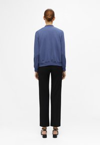 Blauwe bomberjack met elastische manchetten en tailleband, gecombineerd met zwarte rechte broek. Glad materiaal met een eenvoudig, strak ontwerp.