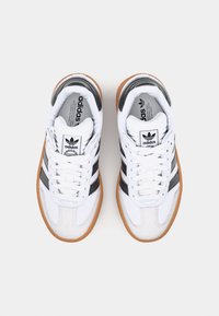 Vita sneakers med svarta ränder, som har en texturerad överdel i mocka och läder, gummisula och klassisk snörning.