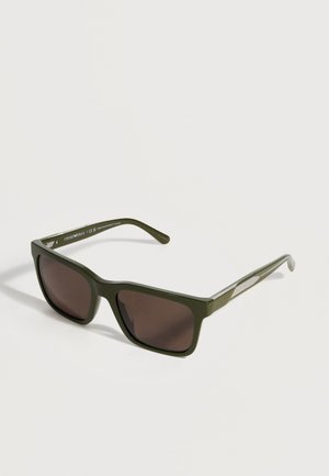 Green rectangular sunglasses with dark lenses resting on a white surface, showing left temple arm detail and subtle brand markings.