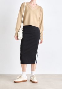 Beżowy sweter z dekoltem w serek, czarna spódnica midi z białymi i niebieskimi paskami po bokach, białe trampki z brązowymi podeszwami i mała biała torba na ramię.