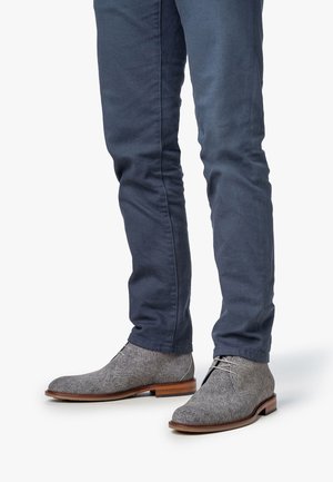Graue, kurze Stiefel aus Leder mit einer runden Zehenpartie, Ledersohle und minimaler Schnürung, kombiniert mit schmalen navyblauen Hosen.