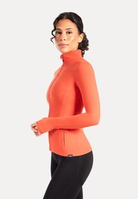 Strakke oranje jas met rits, hoge kraag, lange mouwen en duimgaten. Lichtgewicht stof met vlakke naden, voorzien van zijritspockets.