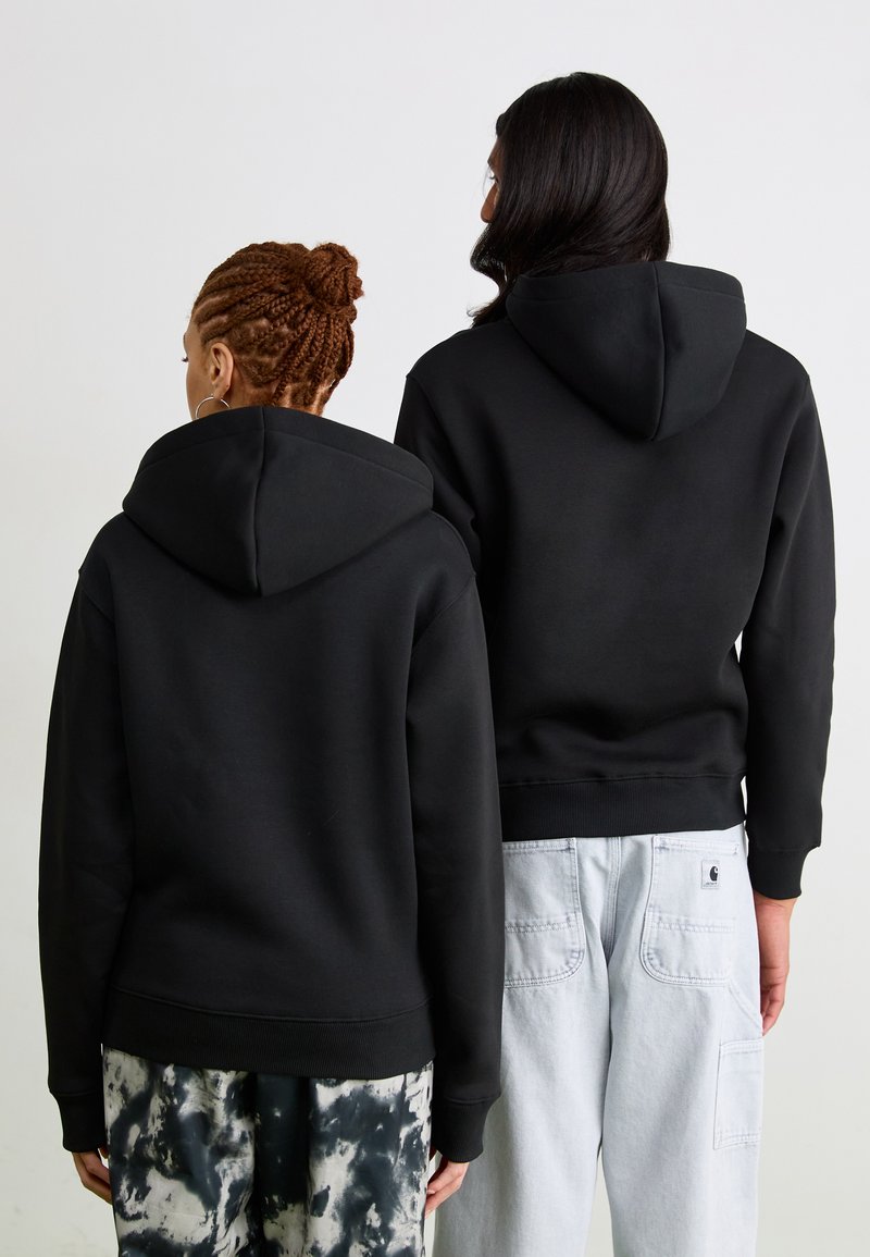 Felpe nere con una texture morbida, dotate di cappuccio, polsini a costine e un taglio rilassato, indossate con pantaloni cargo chiari e pantaloni tie-dye.