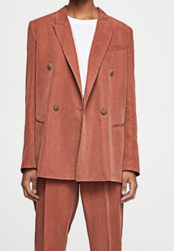 Giacca doppiopetto in corduroy color ruggine. Presenta grandi bottoni, rever a punta e tasche laterali. Abbinata a pantaloni coordinati.