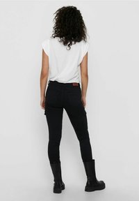 Jeans cargo negros ajustados con bolsillos laterales, diseño de cintura alta y una parche de cuero rojo con el logo en la parte posterior. Combinados con una camiseta blanca.