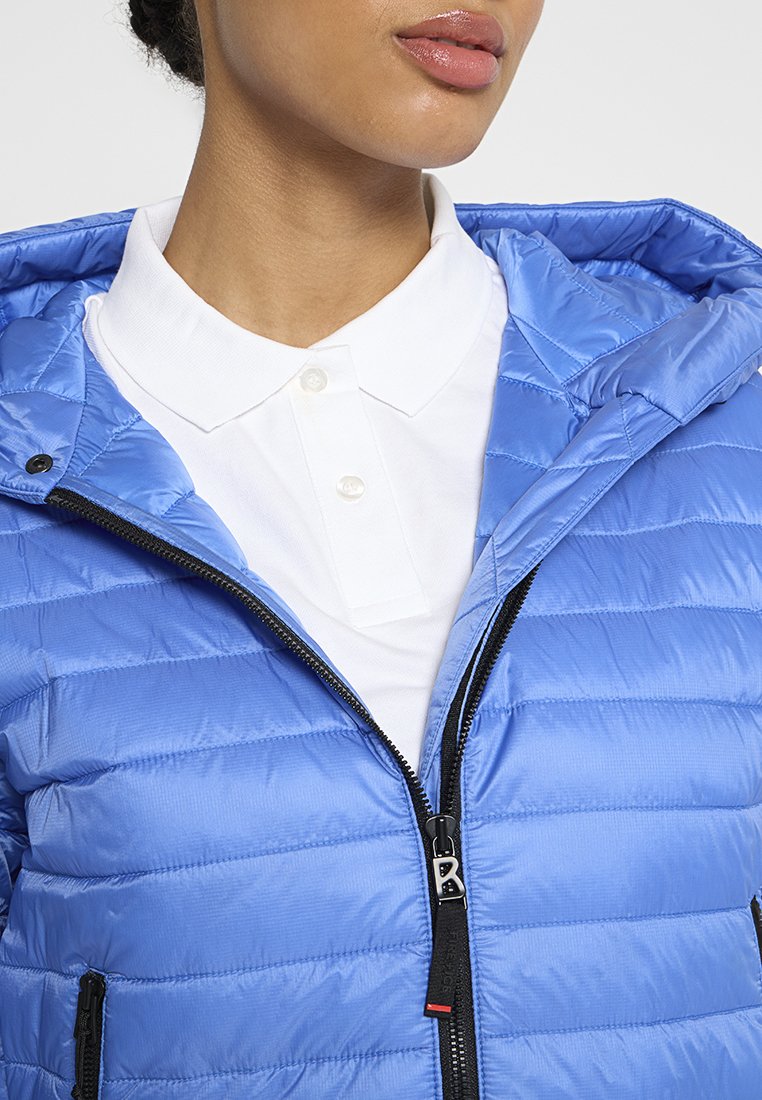 Helle blaue Steppjacke mit gestepptem Design, ausgestattet mit Kapuze, Frontreißverschluss und einem weißen Kragenhemd darunter. Strukturiere Oberfläche.