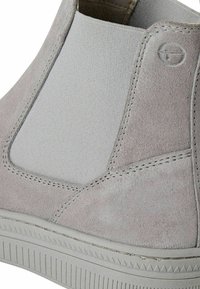 Lichtgrijze enkellaars met een combinatie van soepel suede en gestructureerde stof. Opvallende stiksels en een geribbelde rubberen zool accentueren het ontwerp.